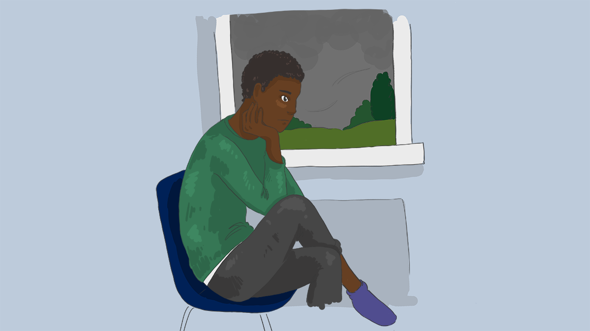 A boy sitting by a window looking sad