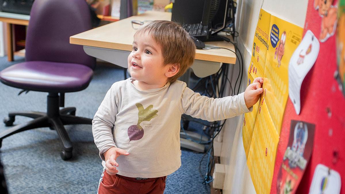 A child smiling while standing next to the BookTrust Storytime voting poster in a library