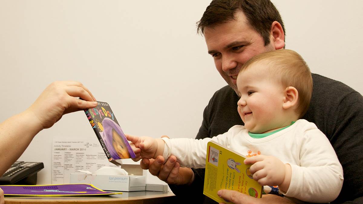 health visitor hands book to dad and baby