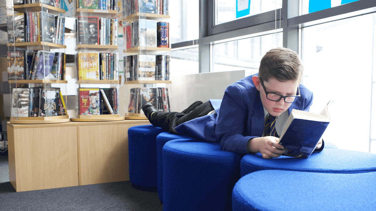 A boy lying down to read in a school library