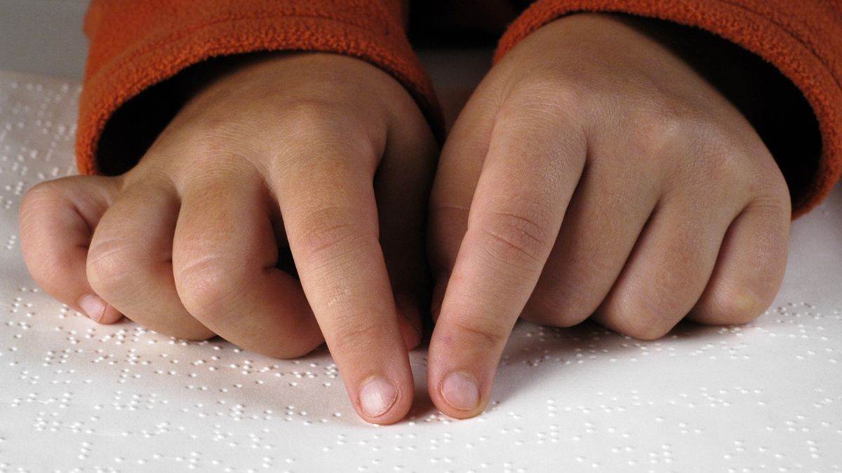 A photograph of a child's hands reading braille