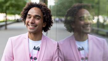 Waterstones Children's Laureate Joseph Coelho smiling outside next to a mirrored building - photo by Vicki Couchman