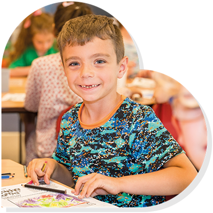 A boy with a Pyjamarama activity sheet smiling in a classroom