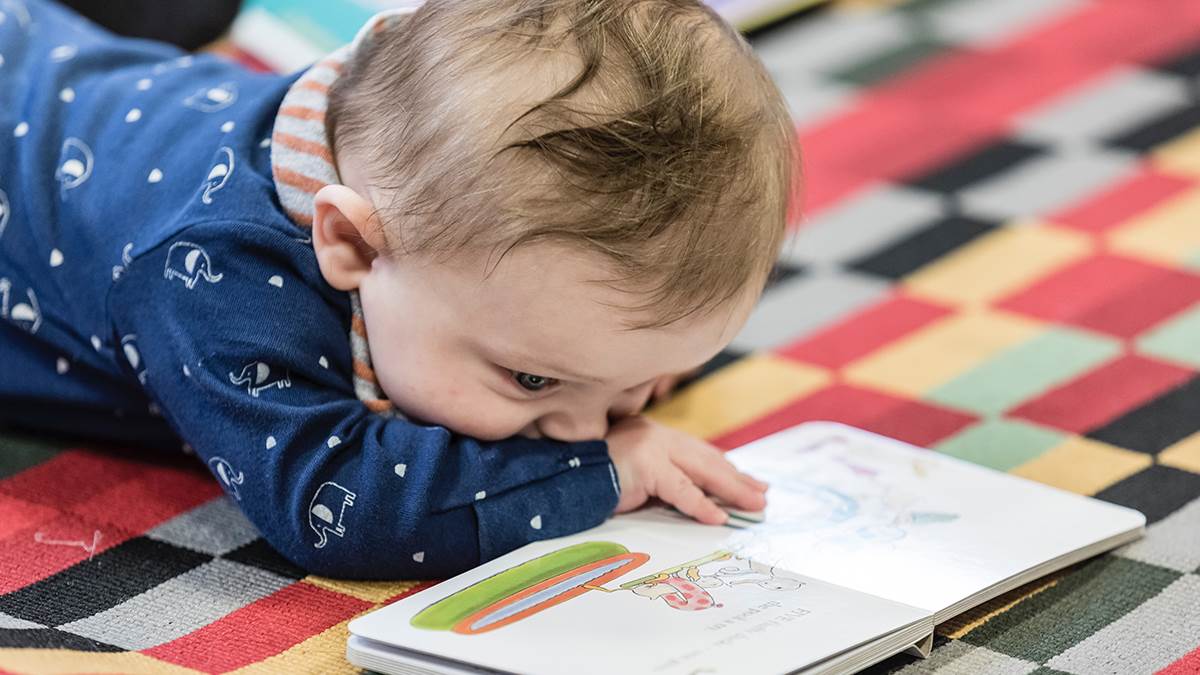 Baby lying on floor looking at book