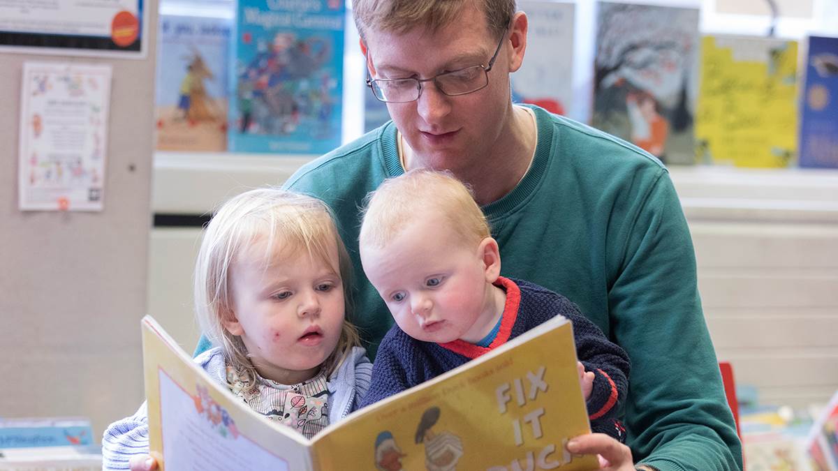 A photo of a dad reading to two children in the library