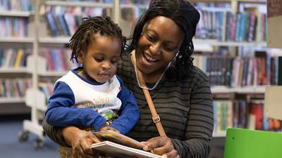 A mother holding her child as they look at a book together in the library