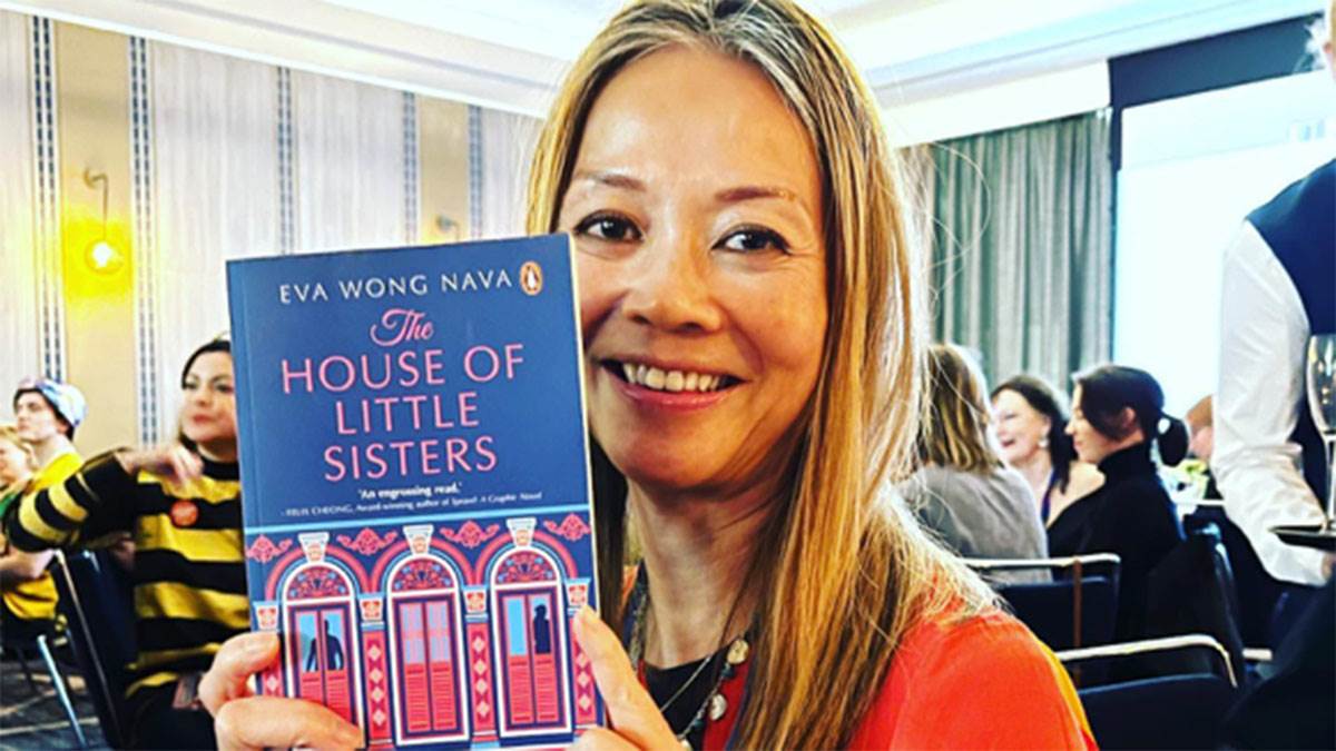 Eva Wong Nava holding up her book The House of Little Sisters