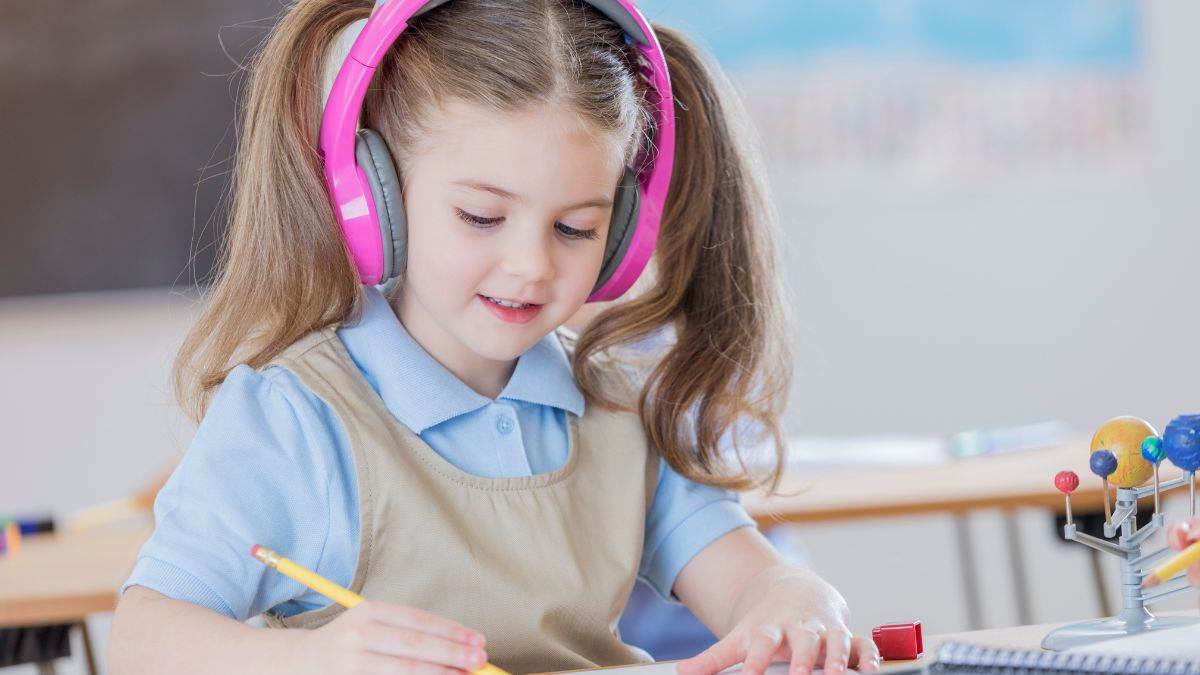 A child in a classroom listening to headphones and writing