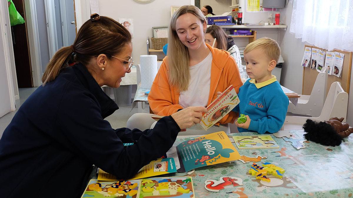 An early years worker sharing a BookTrust pack with a mum and child