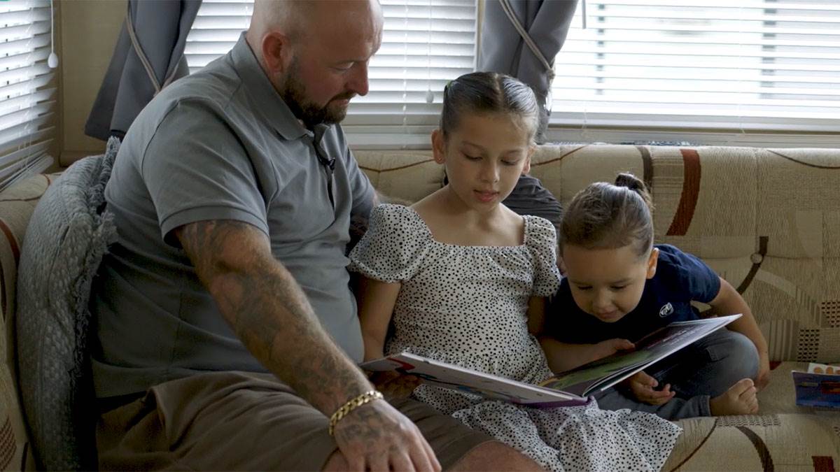 A photo of a man and two children reading together on a sofa