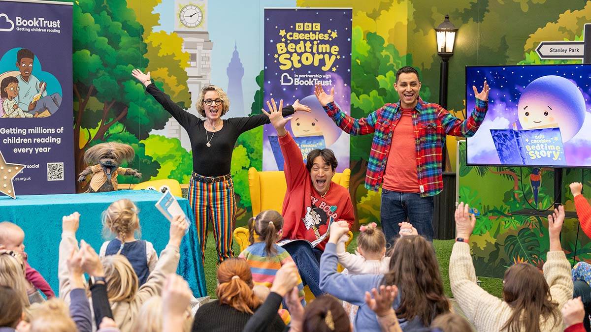 Carlos Gu, Ben Cajee and a sign language interpreter cheering in front of a group of cheering children in Blackpool Central Library