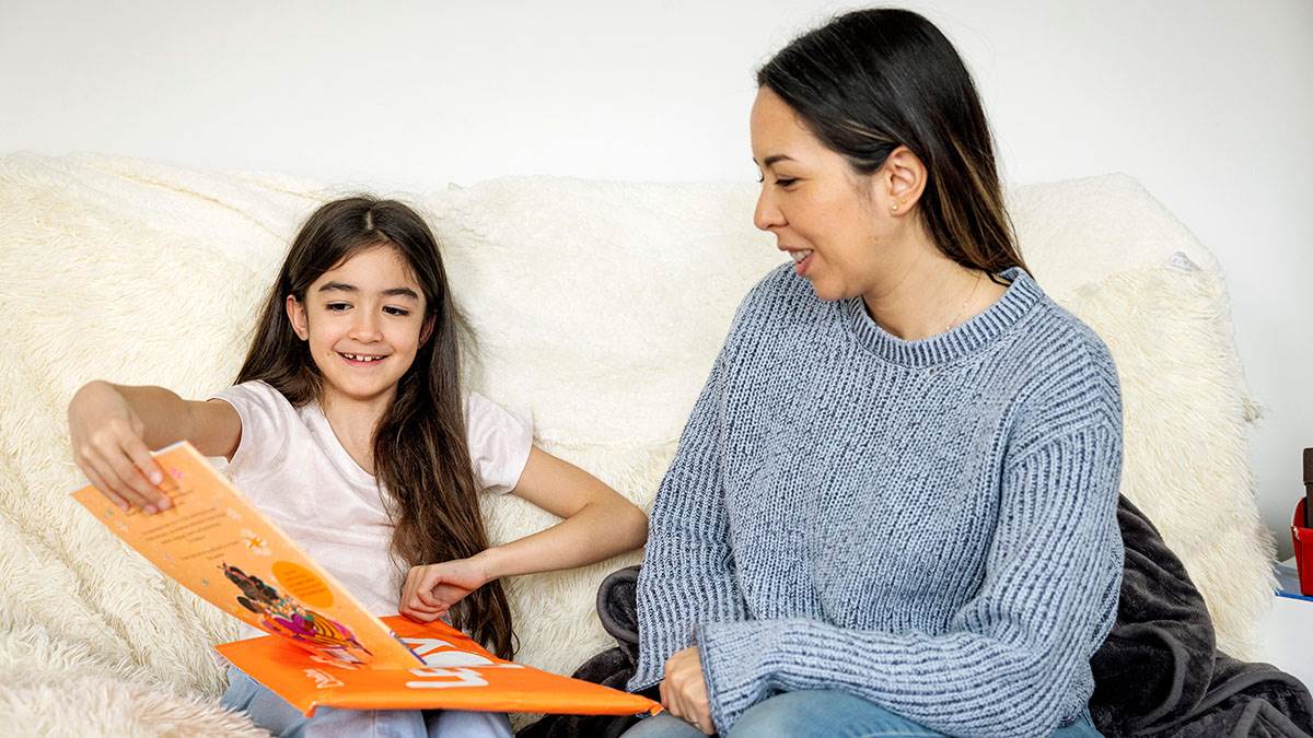 A photo of a girl excitedly taking out the contents of a Letterbox Club parcel; she is sitting on a sofa next to a smiling woman