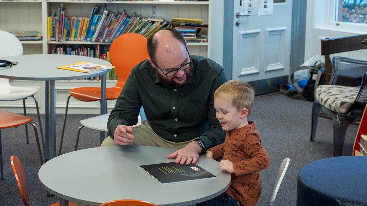 BookTrust NI's Chris Eisenstadt and his son in a library with one of the BookTrust Storytime books