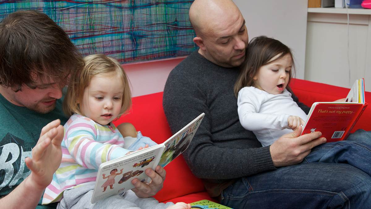 Two dads reading with their daughters