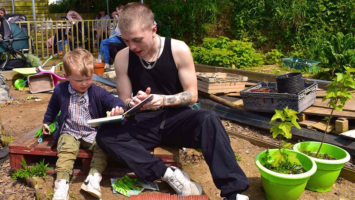 Dad Louie and his son Tommy sharing a story as they sit on an allotment, with other families in the background