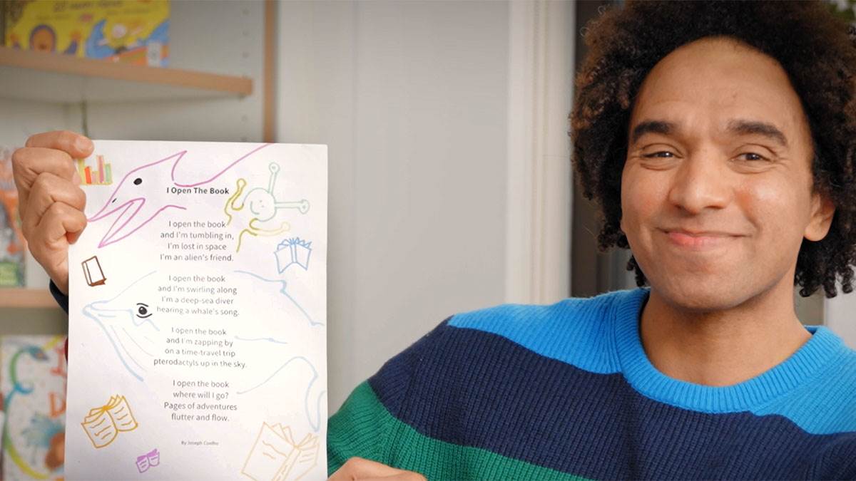 Joseph Coelho smiling as he holds up a poem he has written