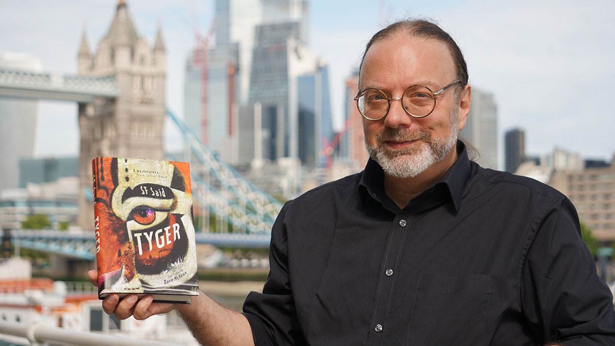 SF Said standing in London holding up his book Tyger, with Tower Bridge in the background